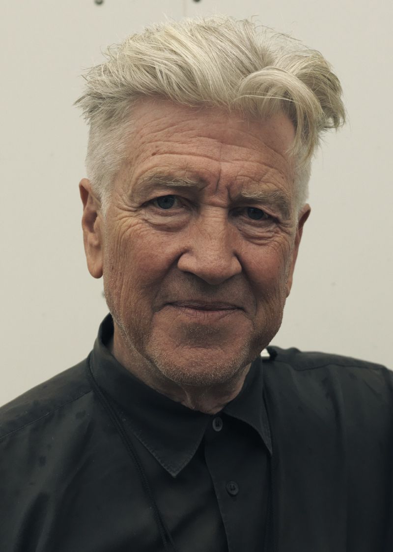 Close portrait of David Lynch in later life, with swept white hair and a black shirt.