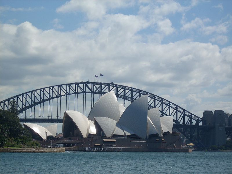 The finished Sydney Opera House seen across the water from Farm Cove, with the Harbour Bridge arch behind it