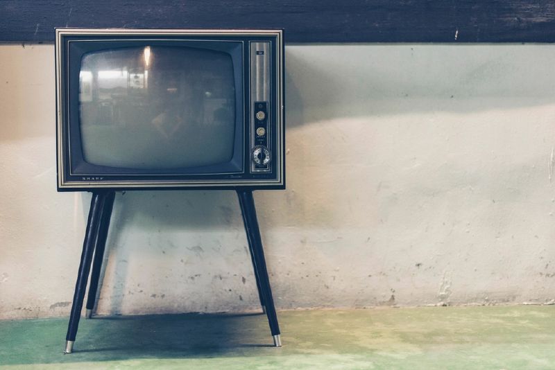 An old television set on thin legs stands against a plain wall.