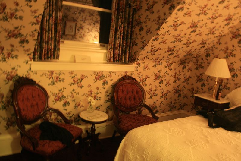 An old-fashioned bedroom with floral wallpaper and two Victorian chairs.