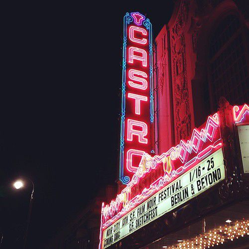 The red neon vertical sign of the Castro Theatre at night, above a marquee listing the Noir City film noir festival