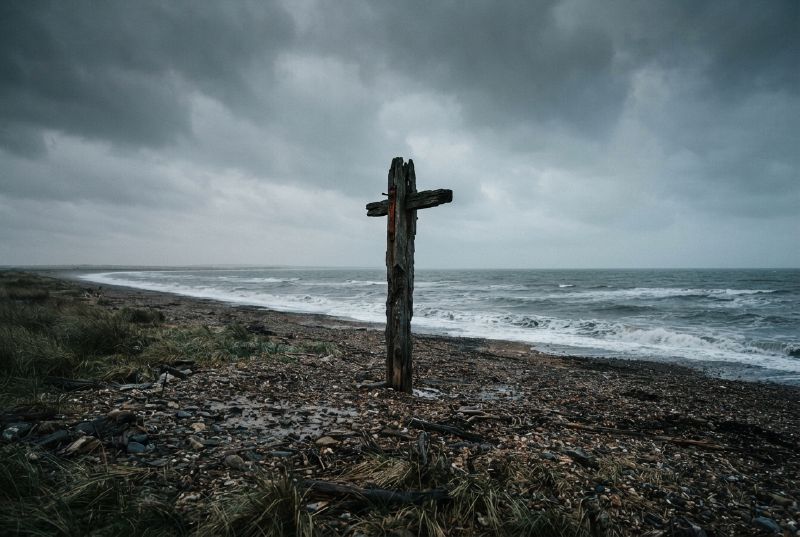 A weathered wooden post stands on a shingle beach under a storm sky.