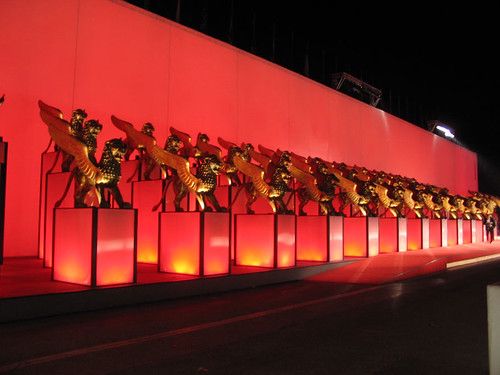 A row of winged golden lion statues on lit red plinths against a red wall at night.