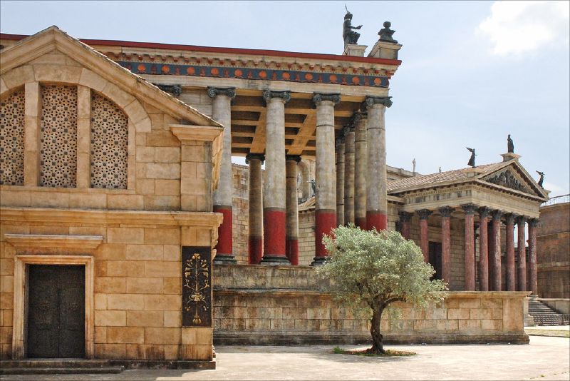 A film set built at Cinecittà studios in Rome, with Roman temple columns painted red and an olive tree in the foreground.