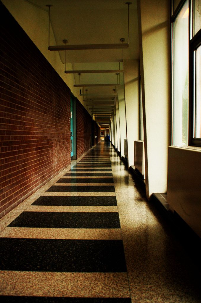 A long brick corridor with sunlight falling through tall windows.