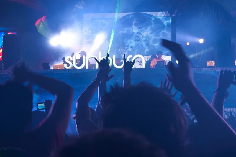 A crowd raises its hands towards a DJ stage under blue light and lasers at the Sunburn Festival in Goa.
