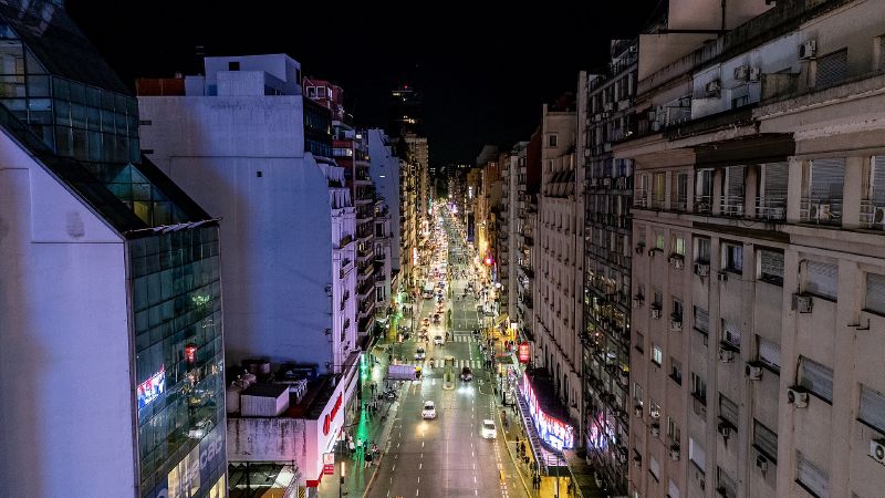 A long city avenue at night seen from above, lined with tall buildings and lit shopfronts