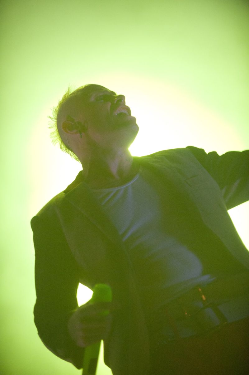 Keith Flint singing on stage at Hultsfred festival in 2011, lit from behind in green light.