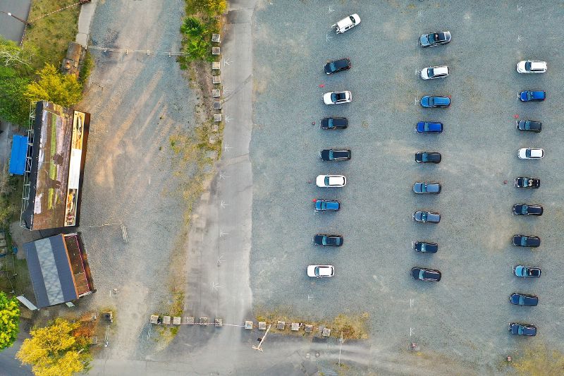 An aerial view of rows of parked cars facing a large outdoor screen at a drive-in cinema.