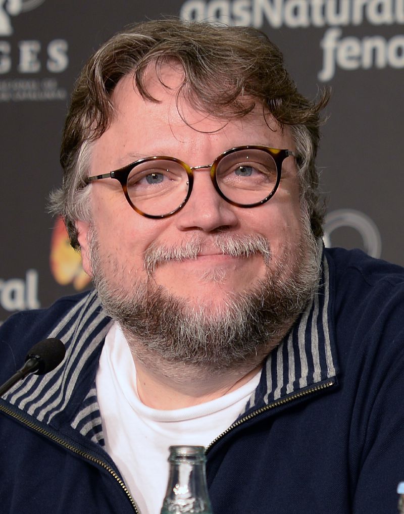 Guillermo del Toro, in round glasses, smiling at a press conference in 2017.