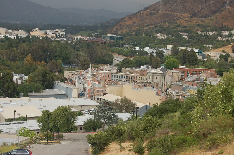 Rooftops and a clock tower of a film-set town on a studio lot, with wooded hills behind.